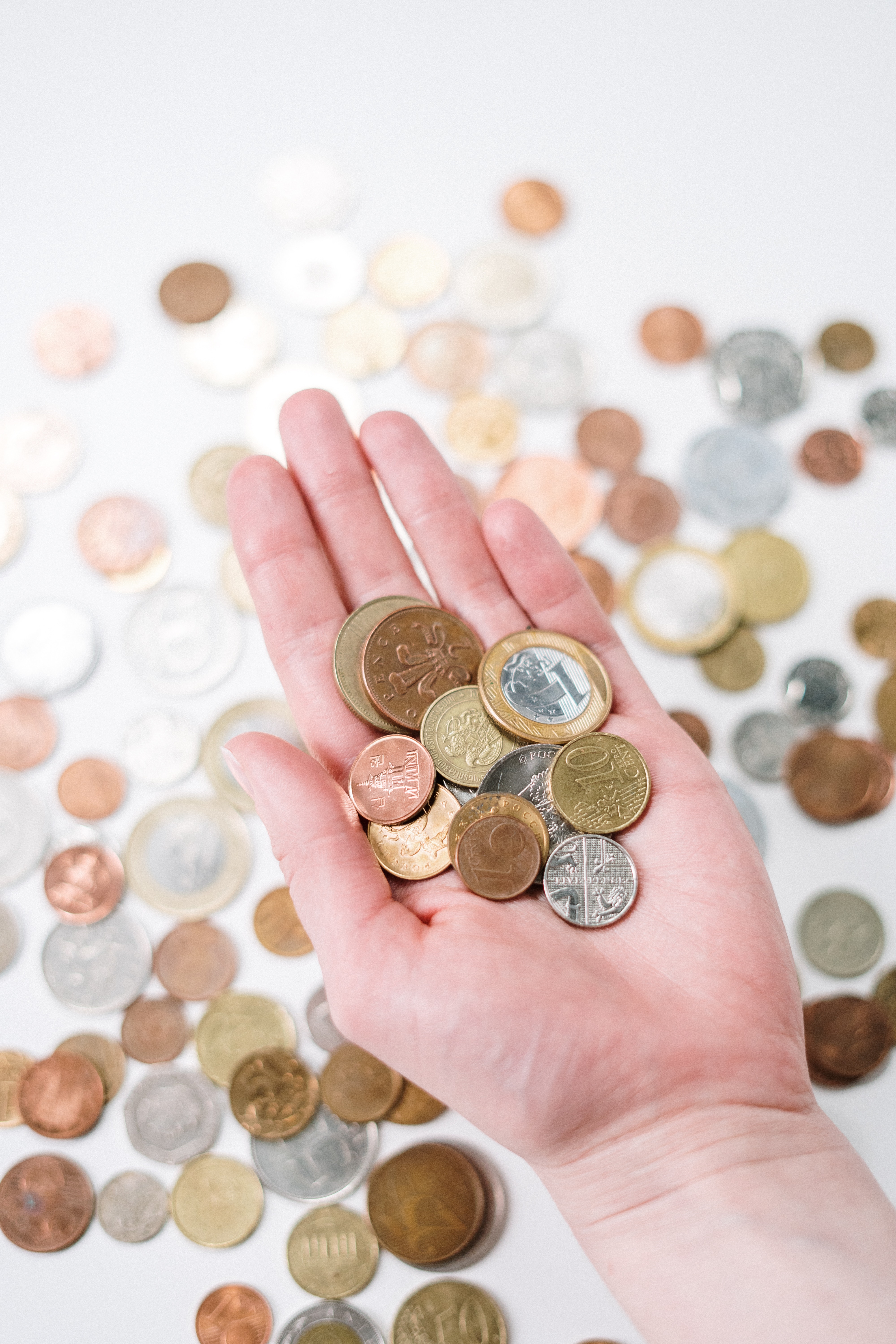 Image of various coins on a white surface, along with a hand holding several coins in its open palm.